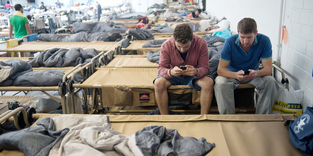 Zwei syrische Flüchtlinge chatten mit ihren Smartphones mit ihren Familien