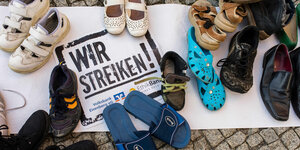 Ein Transparent mit dem Aufdruck "Wir streiken" und dem Logo der Volksbanken liegt auf dem Boden, darauf stehen verschiedene paar Schuhe