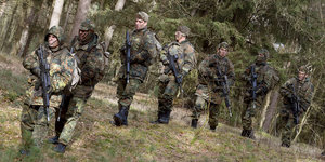 Soldaten in Tarnuniformen und mit Gewehren gehen durch den Wald.