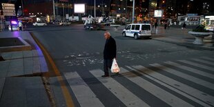 Ein Mann mit einer Plastiktüte läuft abends über einen Zebrastreifen.