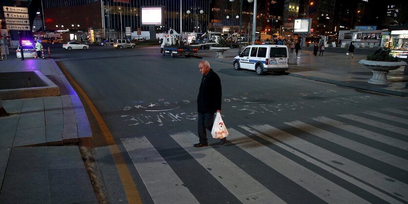 Ein Mann mit einer Plastiktüte läuft abends über einen Zebrastreifen.