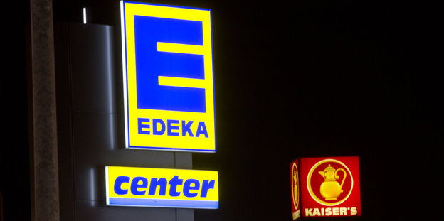 Zwei Werbetafeln im Dunkeln, sie leuchten. Auf einem steht Edeka Center, auf dem anderen ist eine Kanne und das Wort Kaiser's zu lesen