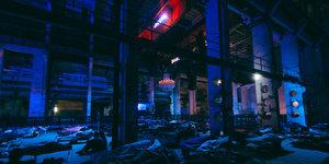 Großer Saal in blaues Licht getaucht, ganz viele, von Schlafenden belegte Pritschen füllen den Raum.