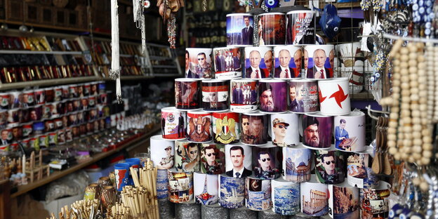 Tassen mit Porträts von Bashar Al-Assad, Wladimir Putin und Hassan Nassrallah sind zu einer Pyramide aufgestapelt.