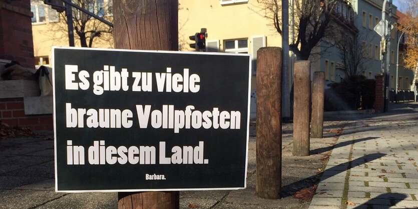 Holzpfosten hintereinander, an einem ein Schild mit der Aufschrift: "Es gibt zu viele braune Vollpfosten in diesem Land."