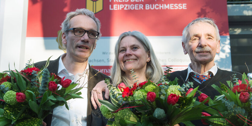 Mann mit Brille, Frau, Mann nebeneinander, lächelnd, mit Blumensträußen