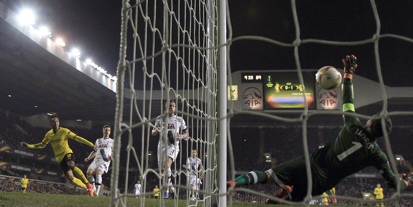 Ein Fußballfeld aus der Torperspektive, ein Ball fliegt Richtung Netz