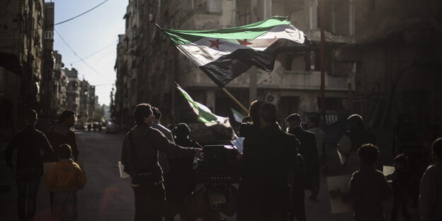 Eine Gruppe von Menschen geht durch einen Straßenzug in Douma. Sie schwenken die syrische Flagge.