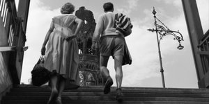 Eine Frau und ein Mann steigen eine Treppe hinauf. Im Hintergrund ist die Gedächtniskirche zu sehen.