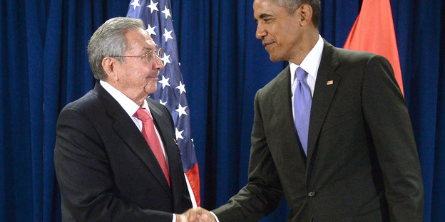 Raul Castro und Barack Obama schütteln sich die Hände vor zwei Flaggen