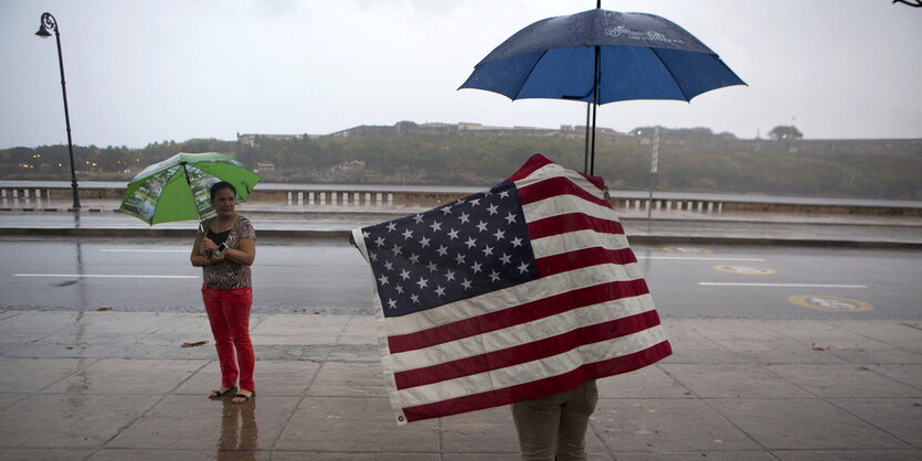 ein Mann mit Regenschirm in eine US-Fahne gehüllt