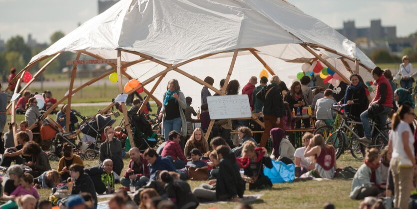 Menschen liegen auf einer Wiese. Hinter ihnen ist eine Kupppel zu sehen.