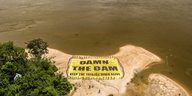 auf dem Ufersand liegt ein großes gelbes Plakat mit der Aufschrift „DAMN THE DAM“