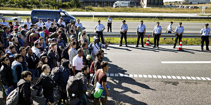 Eine Ansammlung von Menschen auf einer Straße, an der Leitplanke stehen Polizisten