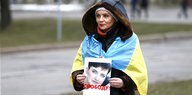 Eine Frau, eingehüllt in eine ukrainische Flagge, hält ein Foto von einer Frau in der Hand