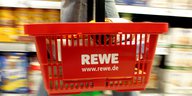 Ein Rewe-Einkaufskorb wird durch einen Supermarkt getragen.