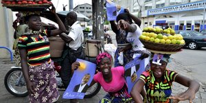 Frauen halten Wahlplakate in der Hand, andere tragen Obstschalen auf dem Kopf