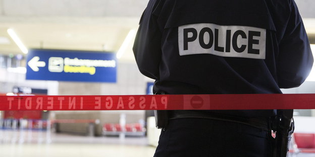 Ein französischer Polizist mit der Aufschrift "Police" auf der Rückseite seiner Jacke vor einem Absperrband