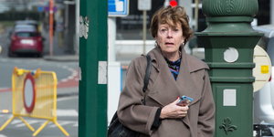 Neelie Kroes steht mit ihrem Smartphone auf einer Straße in Brüssel und schaut erschrocken