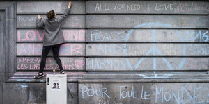 Eine junge Frau malt mit Kreide an eine Wand, auf die unter anderem ein großes Peace-Zeichen gemalt wurde