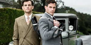 Zwei Männer stehen mit Turnschuhen in der Hand vor einem Auto