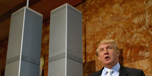 Ein Mann mit blonden Haaren steht neben einem Modell zweier Hochhäuser
