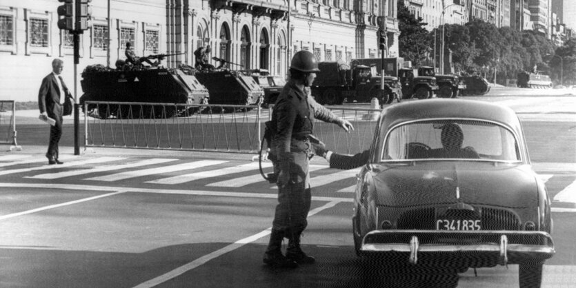 Ein Soldat kontrolliert ein Auto. Weiter hinten stehen Panzer vor einem Gebäude