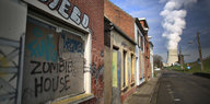 Eine verlassene Häuserreihe, auf einem Brett steht „Zombie House“. Am Ende der Straße ein Kühlturm, aus dem Dampf aufsteigt