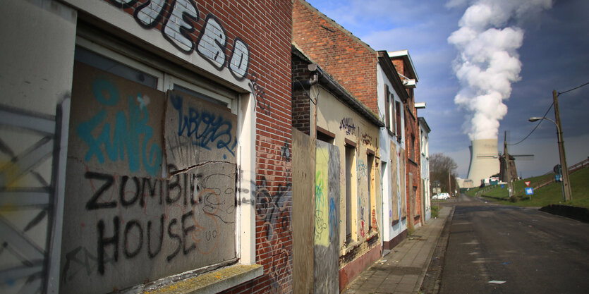 Eine verlassene Häuserreihe, auf einem Brett steht „Zombie House“. Am Ende der Straße ein Kühlturm, aus dem Dampf aufsteigt