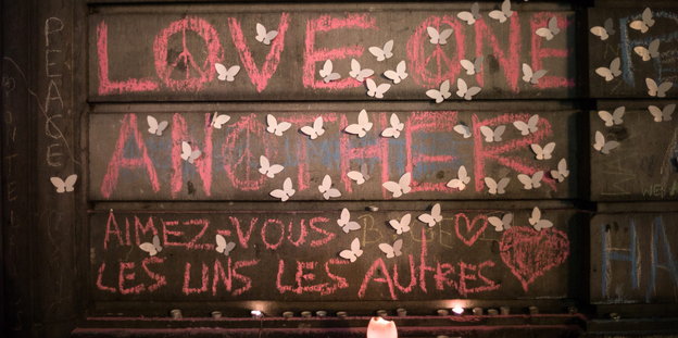 Eine Wand, auf der in pinker Kreide „Love One Another“ steht