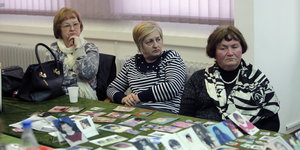 Drei Frauen sitzen hinter einem Tisch, auf dem Fotos von Kriegsopfern liegen