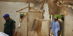 Zwei Männer in einem zerbombten Haus. Holz hängt von der Decke herunter