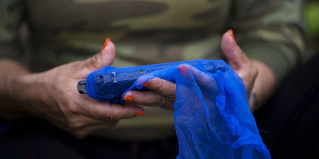 Eine Frau in Camouflage-Kleidung hält eine Waffe in der Hand. Sie ist von einem blauen Netz umhüllt.