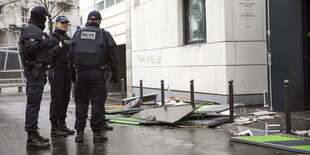 Drei Polizisten stehen auf der Straße. Neben ihnen Gerümpel