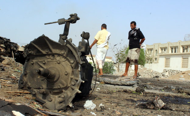 Überreste eines zerbombten Fahrzeugs in einer Straße in Aden, zwei Männer stehen in der Nähe
