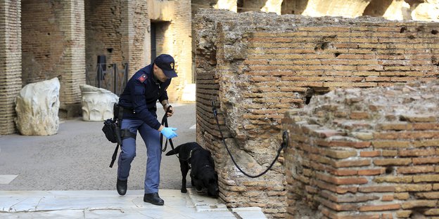 Ein Polizist mit Hund, der schnüffelt an alten Steinen