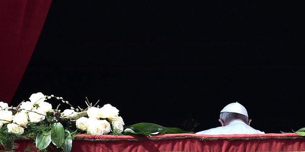 Auf einem balkon liegen weiße Blumen, der Kopf eines Mannes, der Papst, ist von hinten zu sehen
