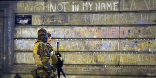 Soldaten in Uniform vor einer beschriebenen Hauswand