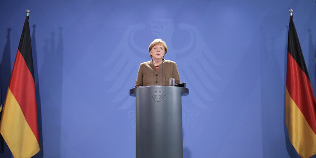 Eine Frau, Angela Merkel, steht an einem Pult, rechts und links von ihr Deutschland-Fahnen