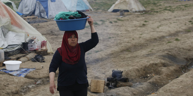Eine Frau trägt in einem Flüchtlingslager eine Plastikschale auf dem Kopf