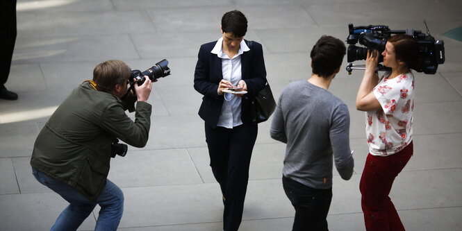 Frauke Petry, umringt von Kameraleuten, läuft über einen Platz und schaut auf ihr Smartphone