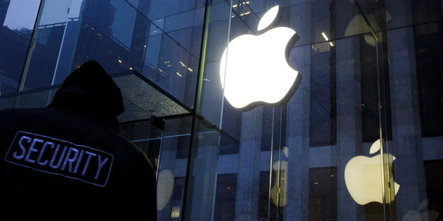 Ein Mensch mit einer Security-Jacke steht vor einem erleuchteten Apple-Symbol