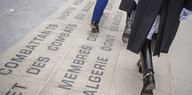Menschen laufen über eine Gedenkplatte in Paris