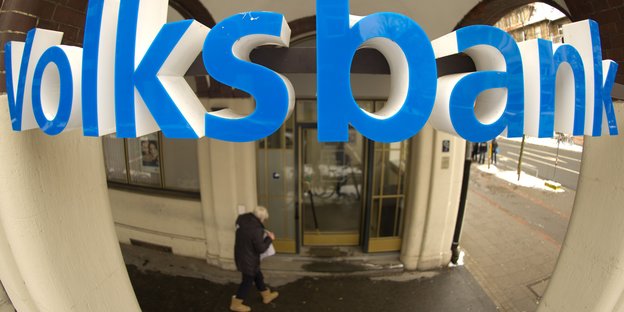 Der blaue Schriftzug „Volksbank“ wölbt sich nach außen, dahinter der Eingang in die Bankfiliale