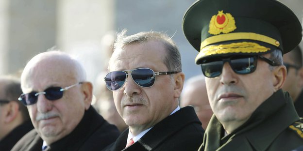 Drei Herren mit Sonnenbrillen und dunklen Anzügen. In der Mitte Präsident Erdoğan