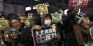 Demonstranten mit Mundschutz halten Schilder mit japanischen Schriftzeichen in die Höhe