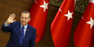 ein Mann mit erhobener Hand vor drei großen türkischen Fahnen
