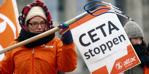 Frau in orangenem Overal hält eine Fahne mit der Aufschrift "Ceta stoppen"