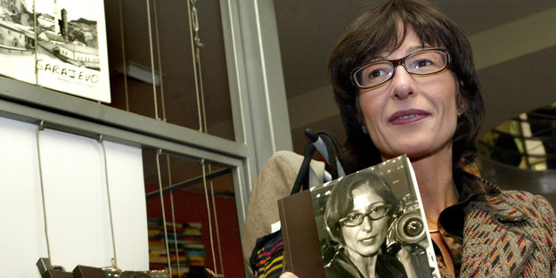 Eine Frau mit dunklen Haaren und Brille hält ein Buch