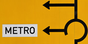 Ein Straßenschild mit zwei Abbiegepfeilen nach links, an einem steht Metro